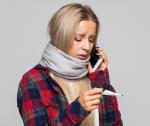 Frau hält Fieberthermometer in der hand und telefoniert