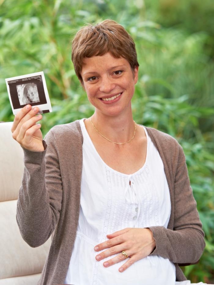 Schwangere Frau hält Ultraschallbild in der Hand.