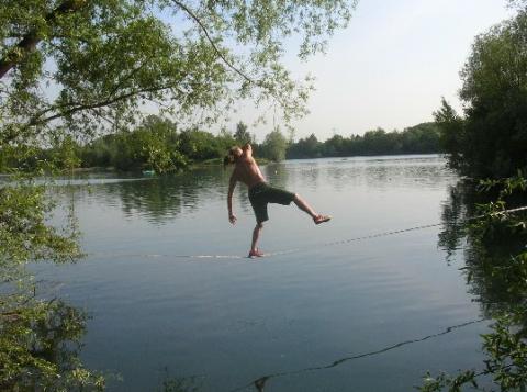 Junger Mann, der auf einer Slackline über einem See balanciert
