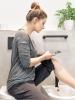 Frau sitzt im Bad und fotografiert mit ihrem Handy ein Hautproblem am Bein